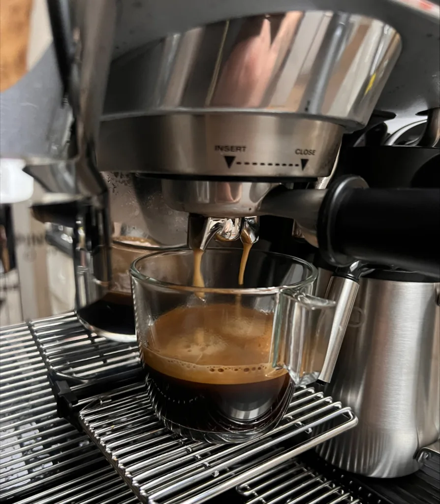 Frischer Espresso fließt in eine klare Glastasse aus einer Kaffeemaschine